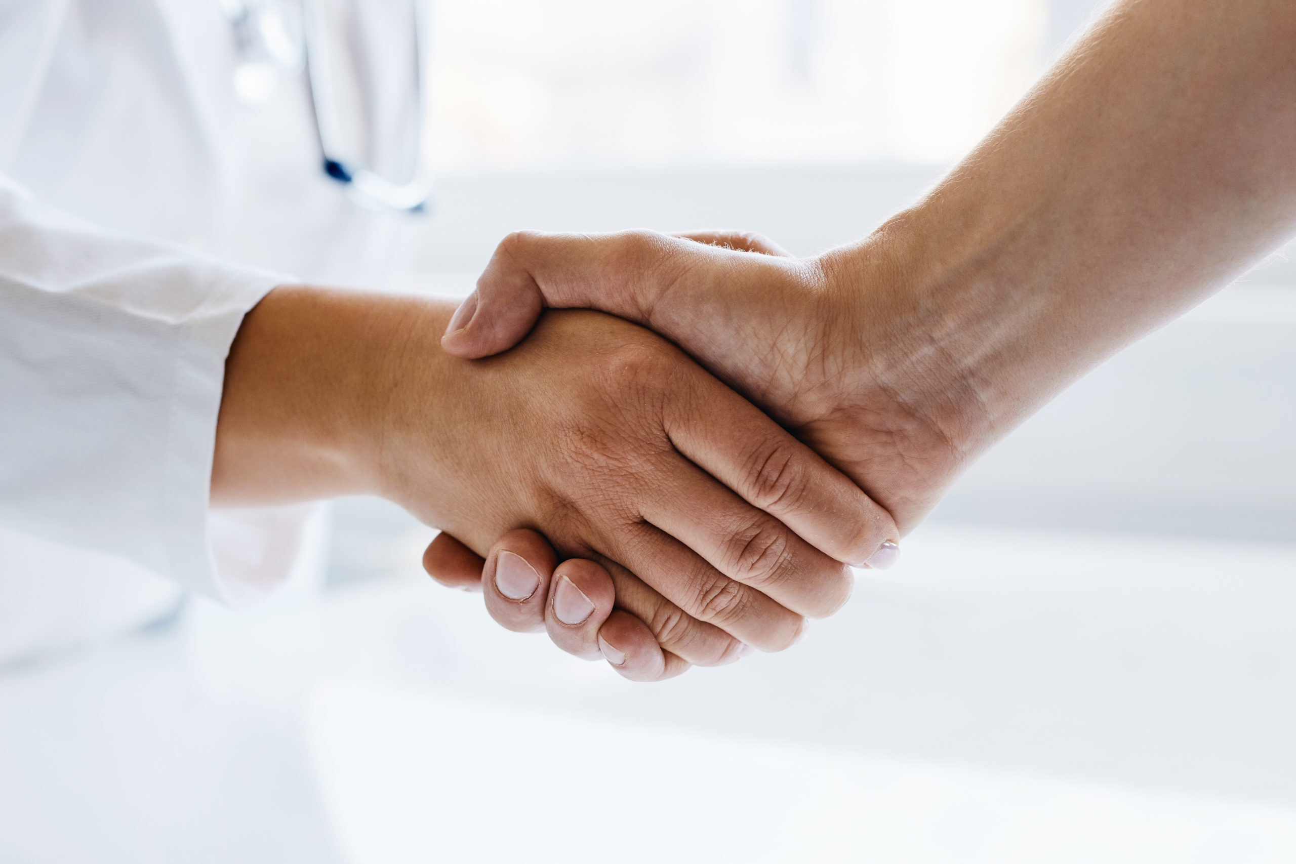 Female doctor shaking hands with man in medical office