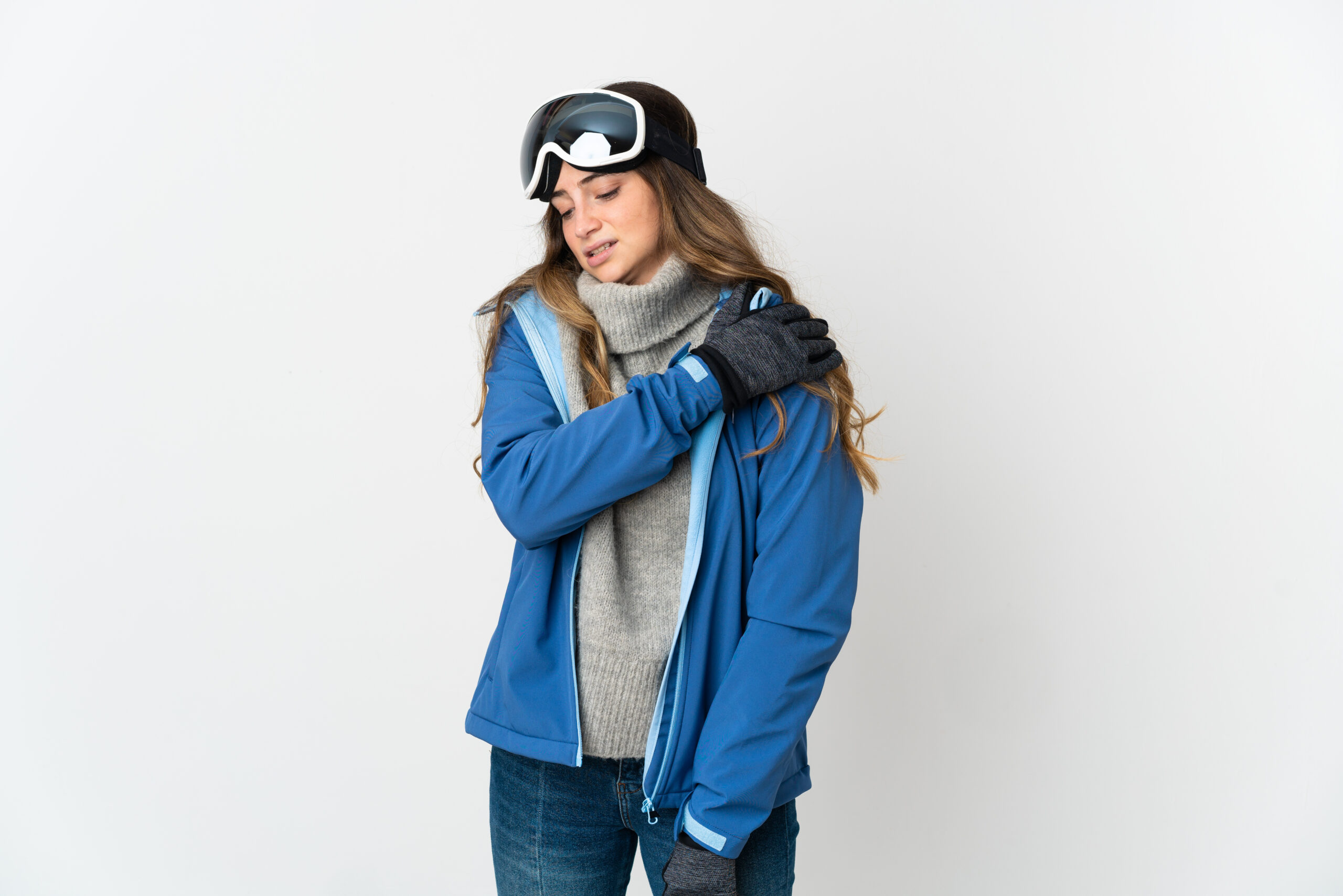 Skier girl with snowboarding glasses isolated on white background suffering from pain in shoulder for having made an effort